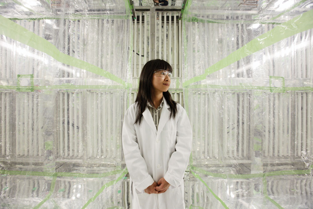 HEI investigator Nga Lee (Sally) Ng wearing a white lab coat and goggles and looking off to her left while standing in front of an environmental chamber at Georgia Tech.